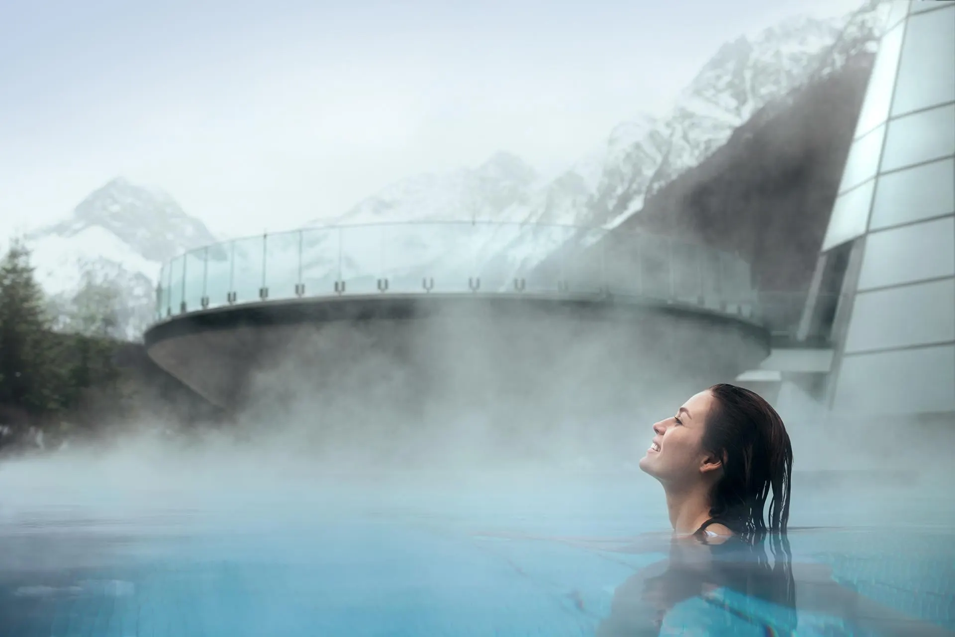 Woman in a steaming outdoor pool below snowy peaks at Aqua Dome