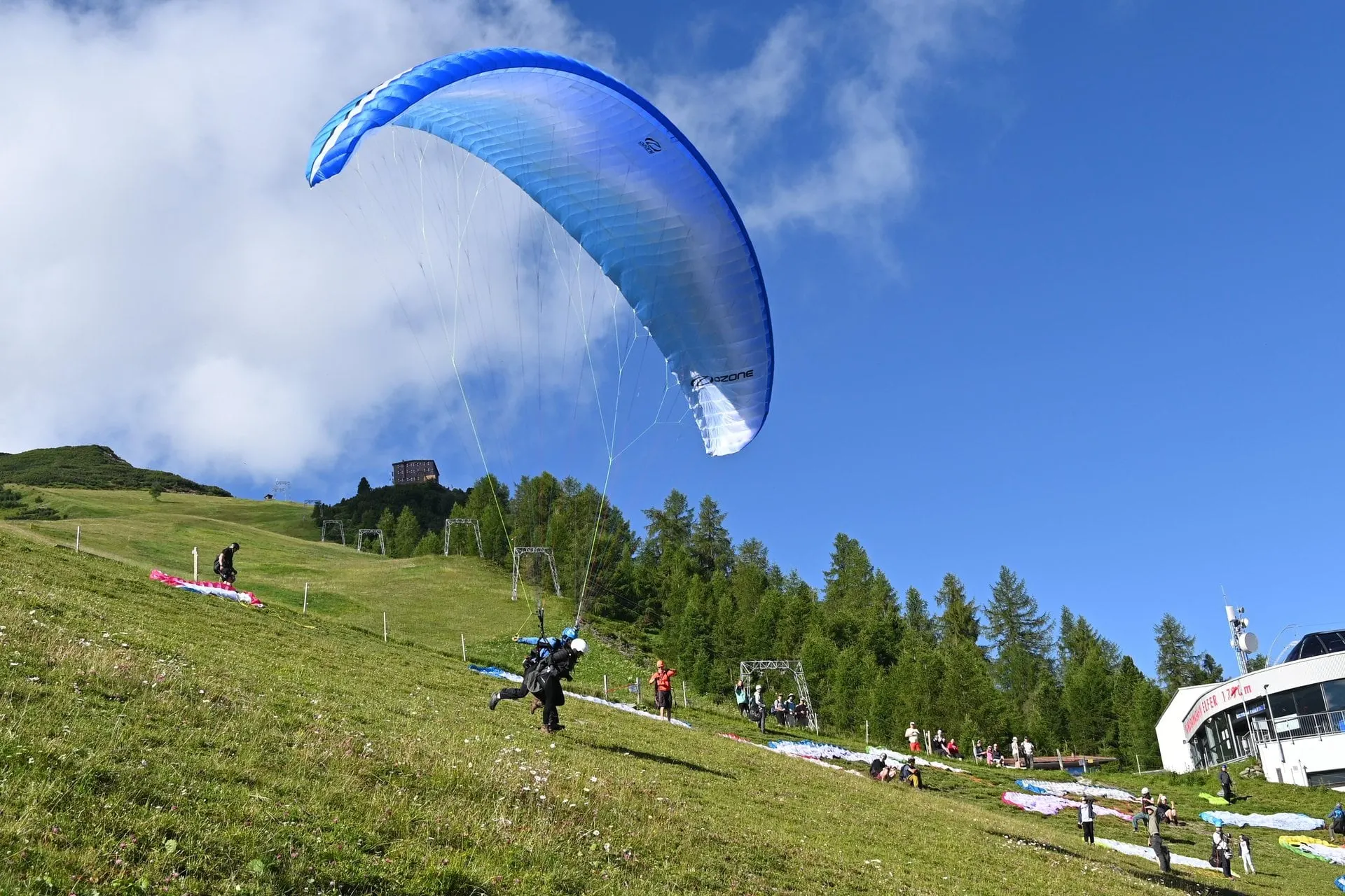 Tandem paraglider taking off from the meadow by the Elfer cable car station