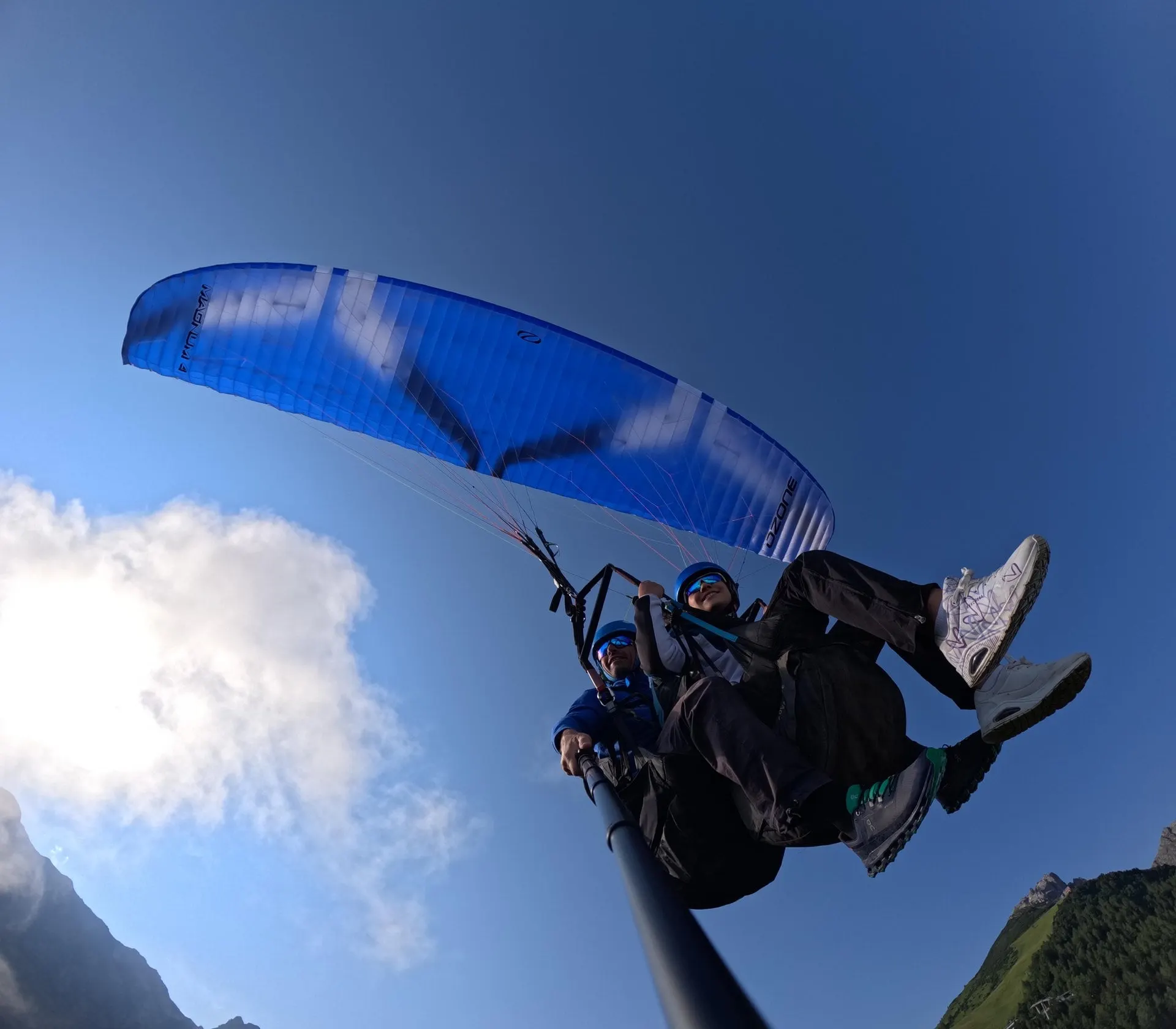 Tandem pilot and passenger flying under a blue wing against the sky
