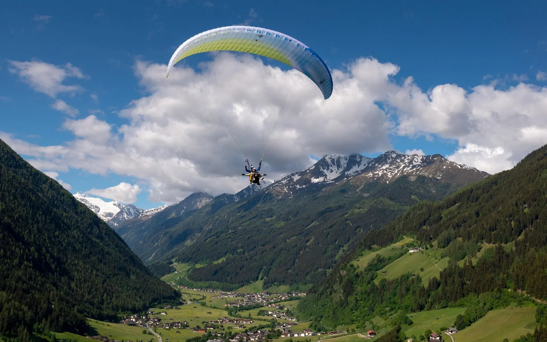 Tandem paraglider above the Stubai Valley with snowy peaks behind