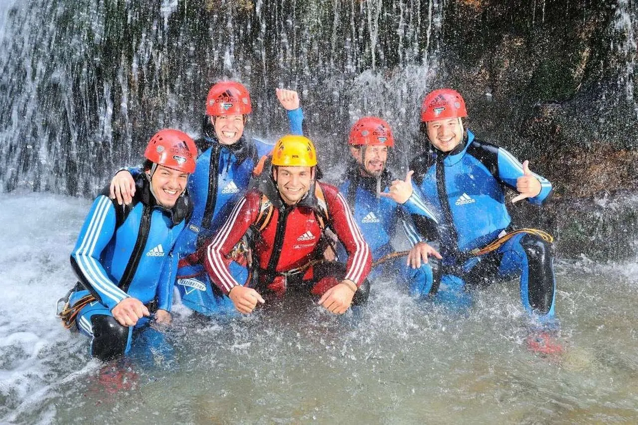 Canyoning group in wetsuits and helmets under a waterfall