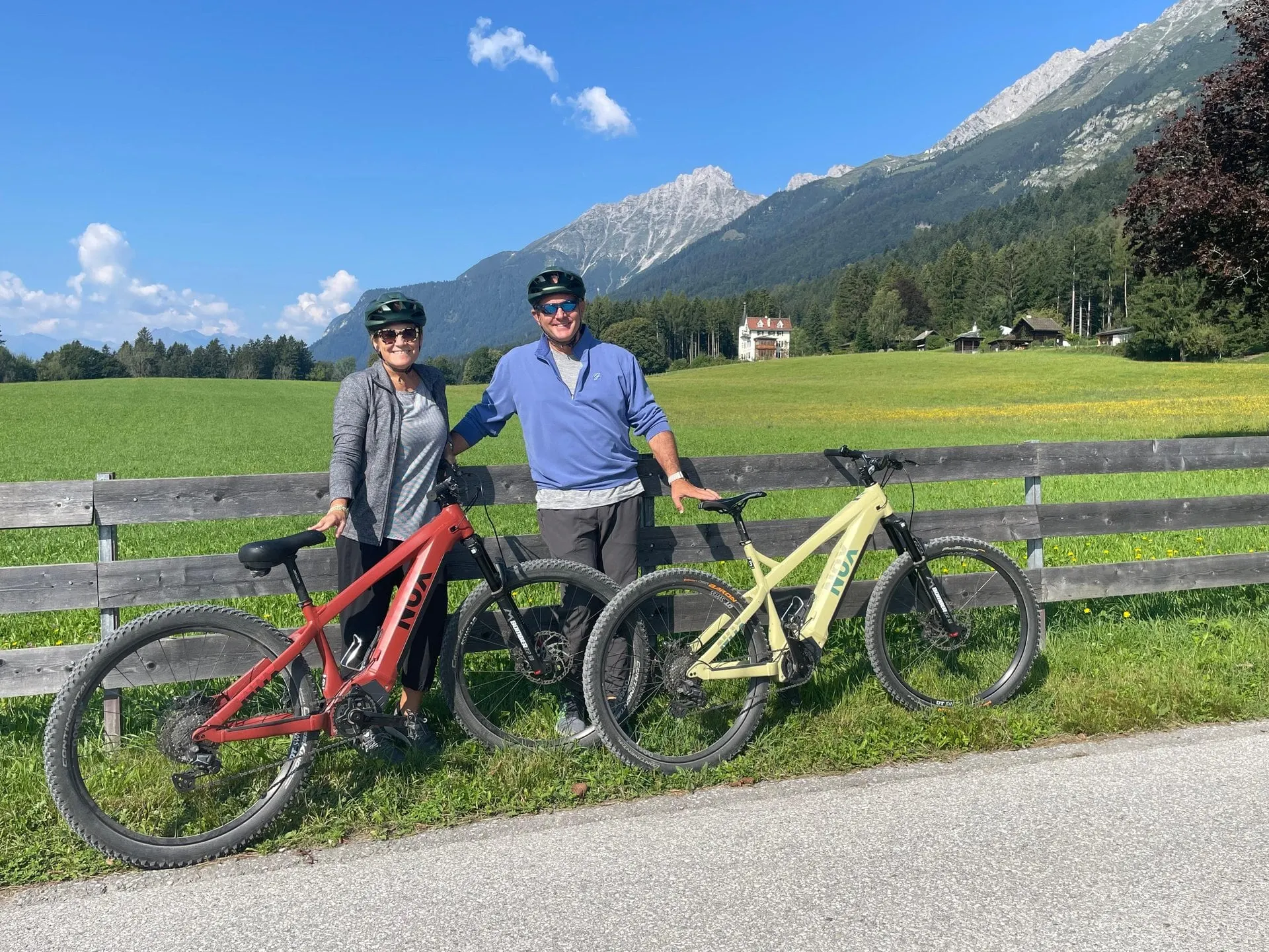 Couple with electric bikes by a meadow fence below the mountains